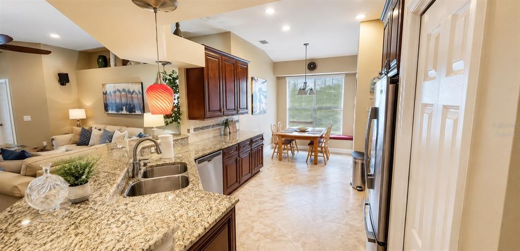 A kitchen with granite countertops and dark wood cabinets opens to a dining area — 4428 HAVELOCKE DRIVE, LAND O LAKES, FL
