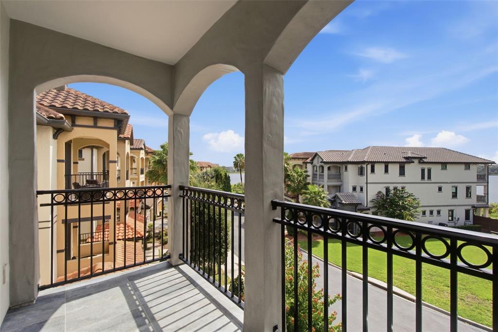 A balcony with black metal railings overlooks a grassy courtyard, apartment buildings, and a lake — 7689 TOSCANA BOULEVARD, ORLANDO, FL