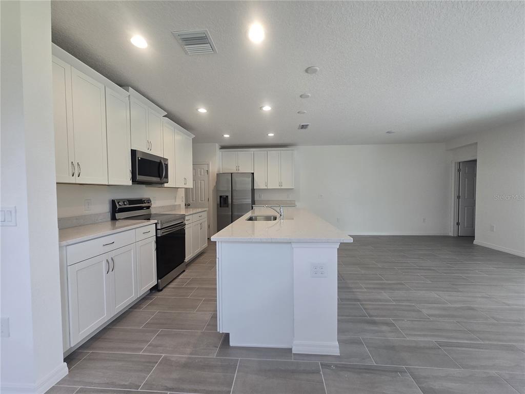 A modern kitchen features white cabinets, stainless steel appliances, a center island, and tile flooring — 2536 STARRY POINT, ST CLOUD, FL