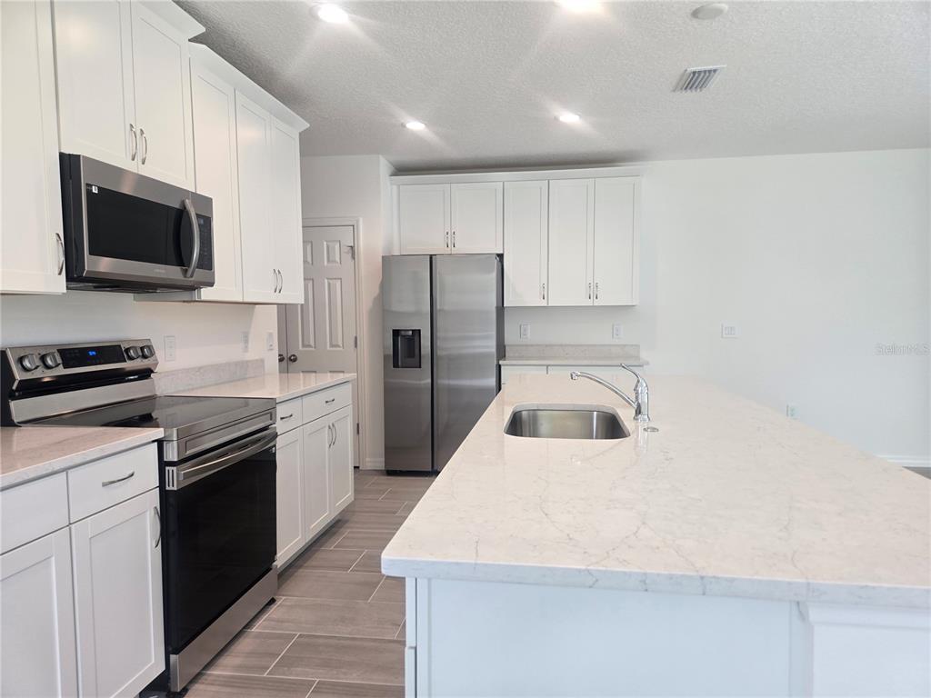 A modern kitchen features white cabinetry, stainless steel appliances, and a large quartz-topped island — 2536 STARRY POINT, ST CLOUD, FL