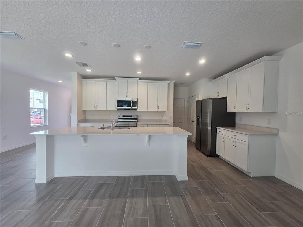 A kitchen features white cabinetry, a large island with a sink, and gray tile flooring — 2536 STARRY POINT, ST CLOUD, FL