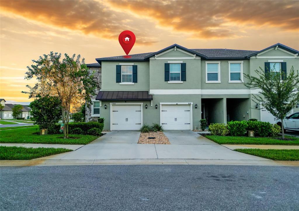 A two-story townhouse with a light green stucco exterior and two attached garages — 7082 RIPPLE POND LOOP, ZEPHYRHILLS, FL