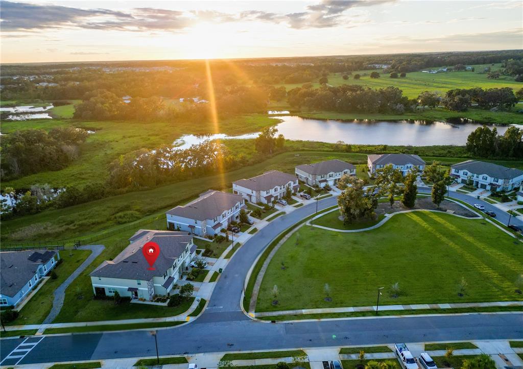 An aerial view shows a suburban neighborhood with houses, a pond, and a sunset — 7082 RIPPLE POND LOOP, ZEPHYRHILLS, FL