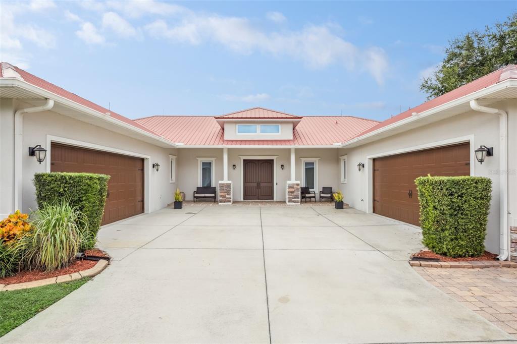 A U-shaped house exterior features a red metal roof, two garage doors, and a driveway — 16909 FLORENCE VIEW DRIVE, MONTVERDE, FL