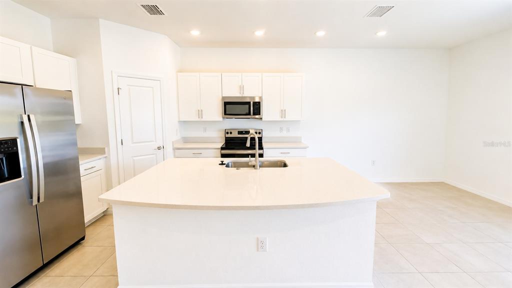 A kitchen with a center island and white cabinets opens to a living area — 5686 ARCHIPELAGO STREET, NOKOMIS, FL