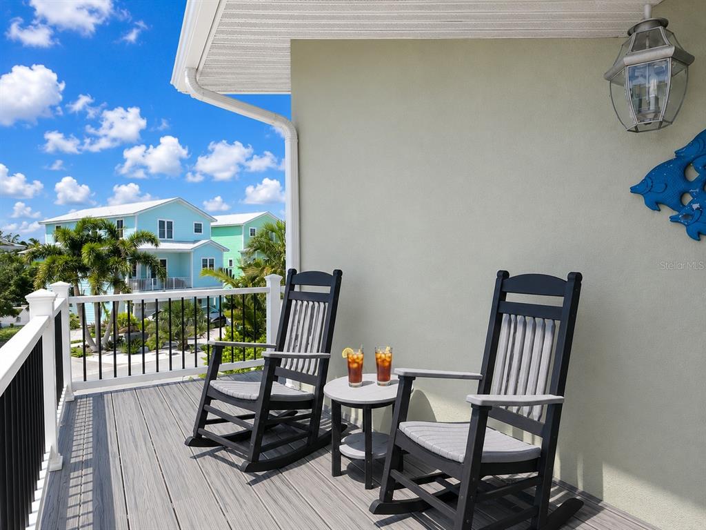 A balcony features two black rocking chairs, a small side table, and a railing — 140 50TH STREET, HOLMES BEACH, FL