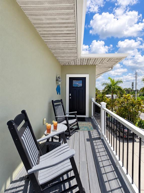 A balcony features two rocking chairs, a small table with drinks, and a black door — 140 50TH STREET, HOLMES BEACH, FL