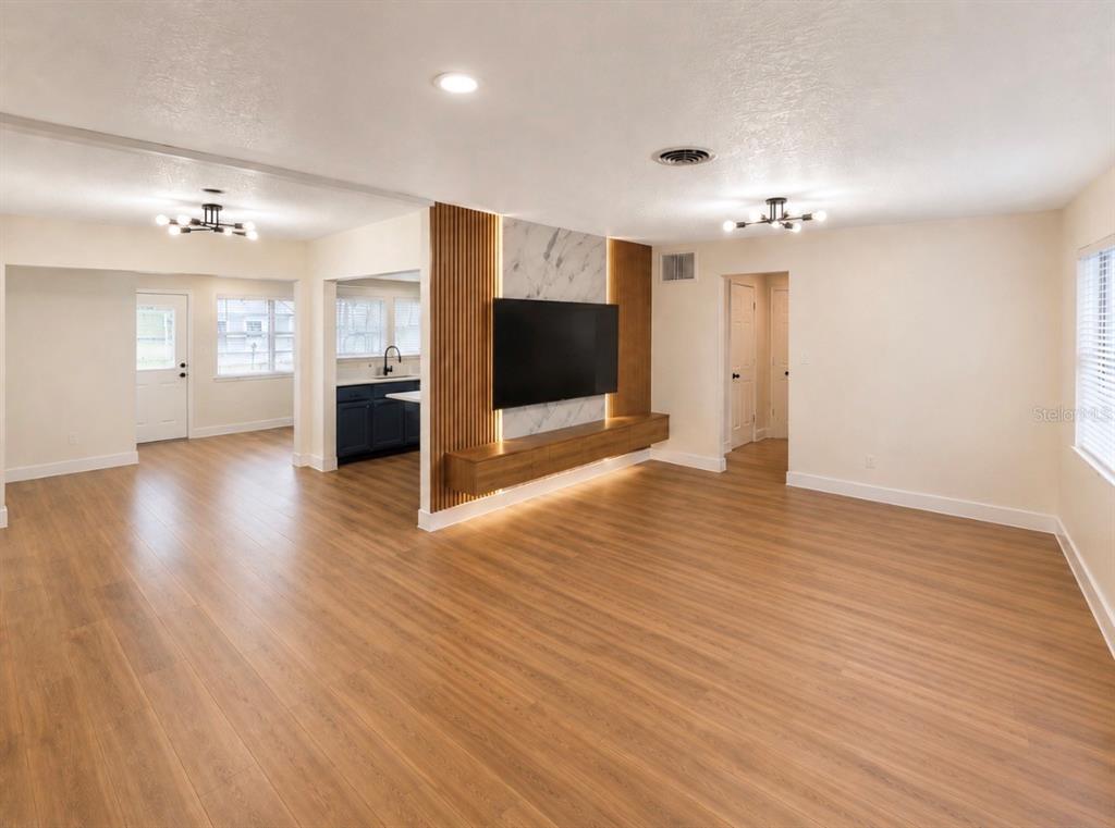 A living room features wood-look flooring, a marble-accented media wall with slat wood, and recessed lighting — 3101 FLOWERTREE ROAD, BELLE ISLE, FL
