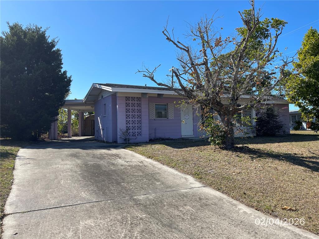 A single-story house with purple siding, a concrete driveway, and a carport under a clear sky — 1708 CAMBRIDGE DRIVE, VENICE, FL