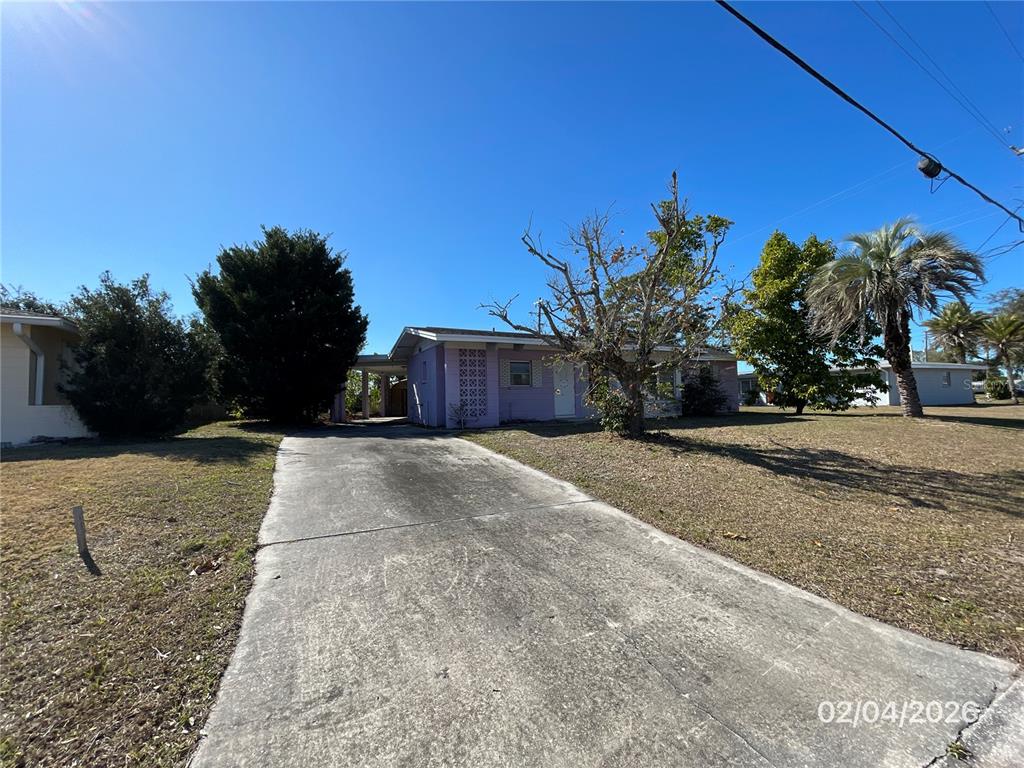 A single-story house with a concrete driveway, a carport, and a large tree in front — 1708 CAMBRIDGE DRIVE, VENICE, FL