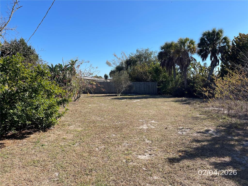 A grassy, vacant residential lot features scattered trees and a wooden fence in the background — 1708 CAMBRIDGE DRIVE, VENICE, FL