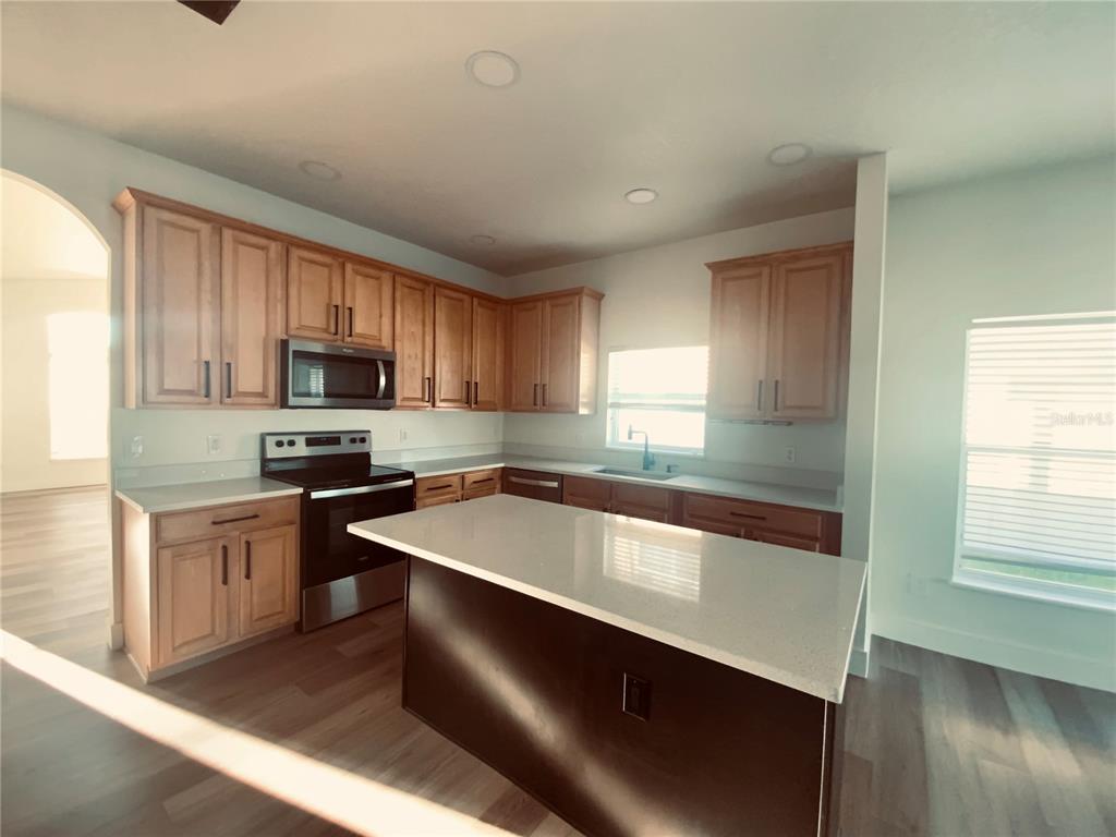 A kitchen features light wood cabinets, a dark kitchen island, and white countertops — 2109 WOODSEDGE DRIVE, KISSIMMEE, FL