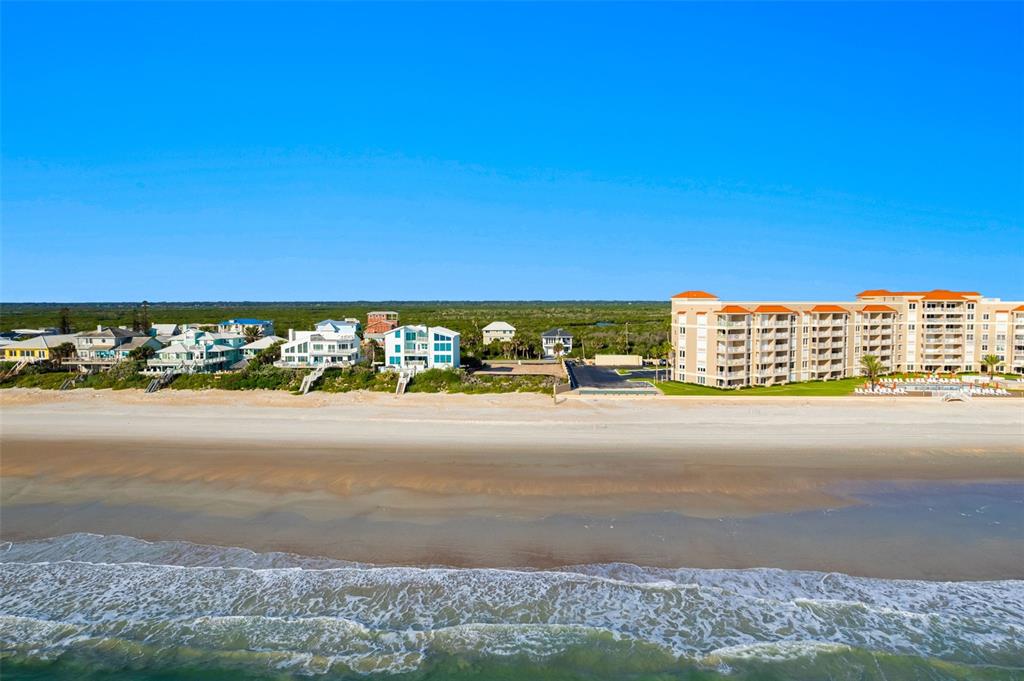 An aerial view shows a sandy beach, ocean waves, and a row of coastal residential buildings — 5575 S ATLANTIC AVENUE, NEW SMYRNA BEACH, FL
