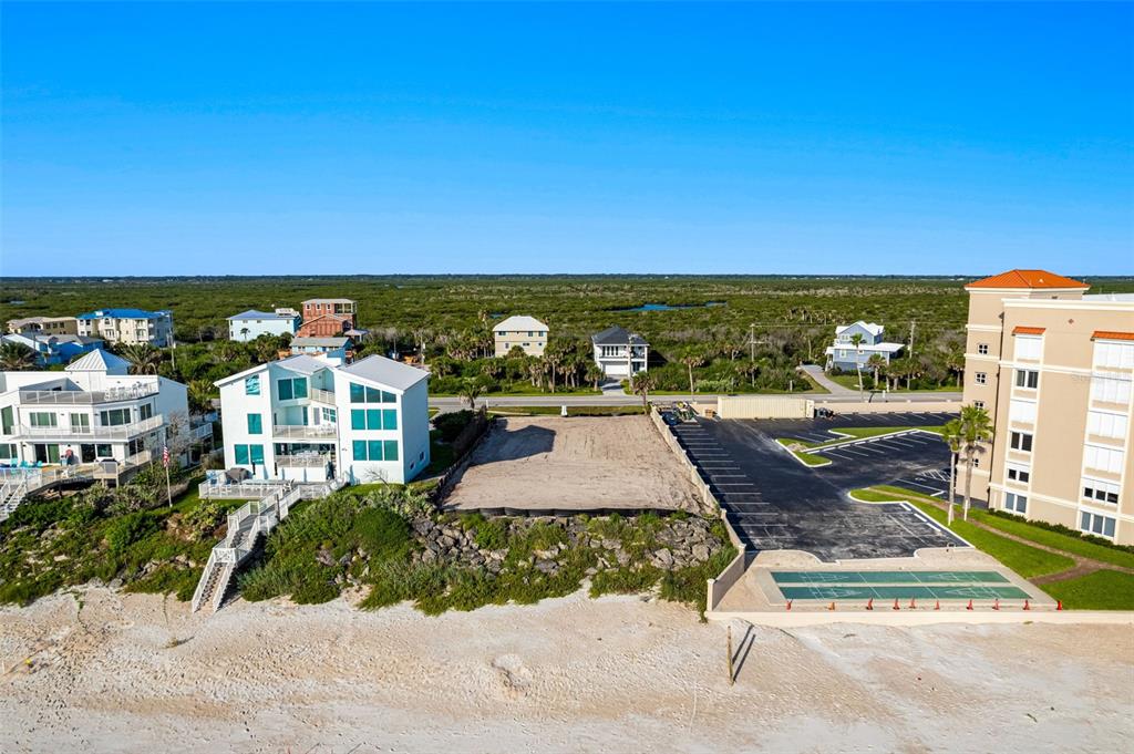 An aerial view shows a vacant beachfront lot situated between a house and a parking lot — 5575 S ATLANTIC AVENUE, NEW SMYRNA BEACH, FL