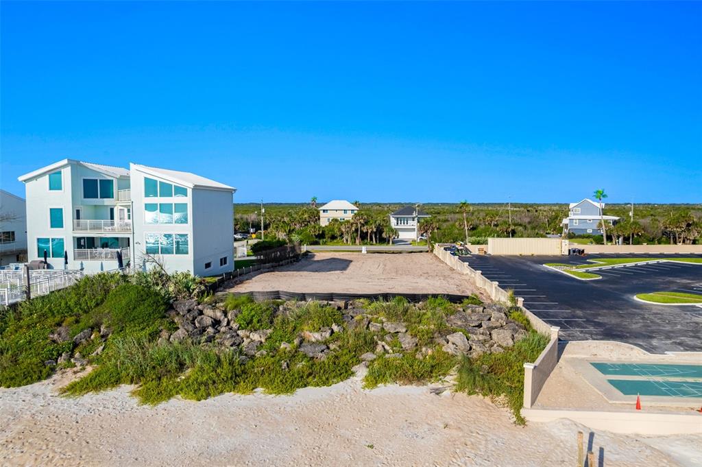 An empty coastal lot sits between a modern white house and a paved parking area — 5575 S ATLANTIC AVENUE, NEW SMYRNA BEACH, FL