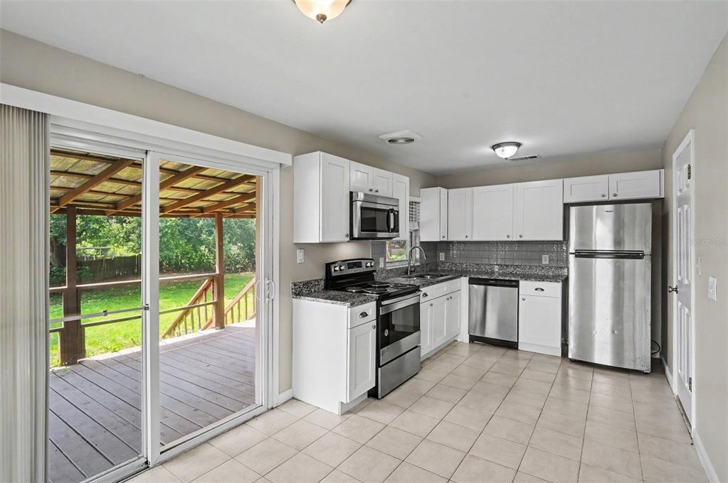 A kitchen with white cabinets, stainless steel appliances, granite countertops, and a sliding glass door — 4406 URBAN COURT, ORLANDO, FL
