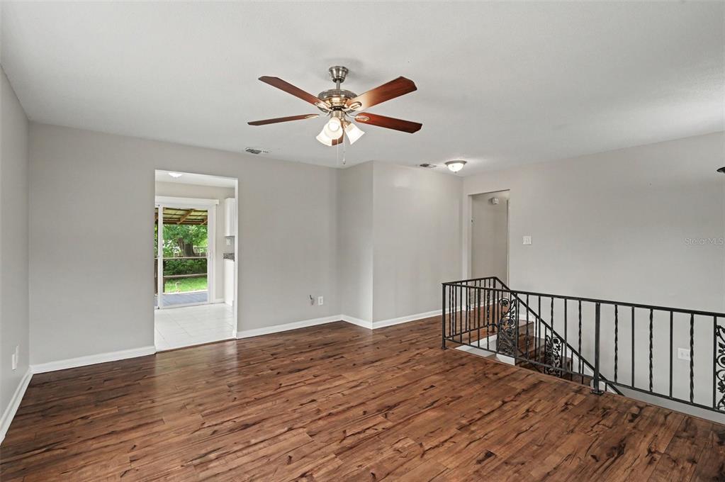 An empty room with wood-look flooring, a ceiling fan, and a staircase with metal railings — 4406 URBAN COURT, ORLANDO, FL
