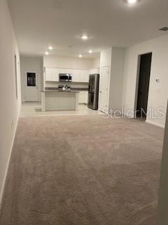 An open-concept living area features beige carpeting and a kitchen with white cabinets and appliances — 2880 POPPY AVENUE, LAKE HAMILTON, FL