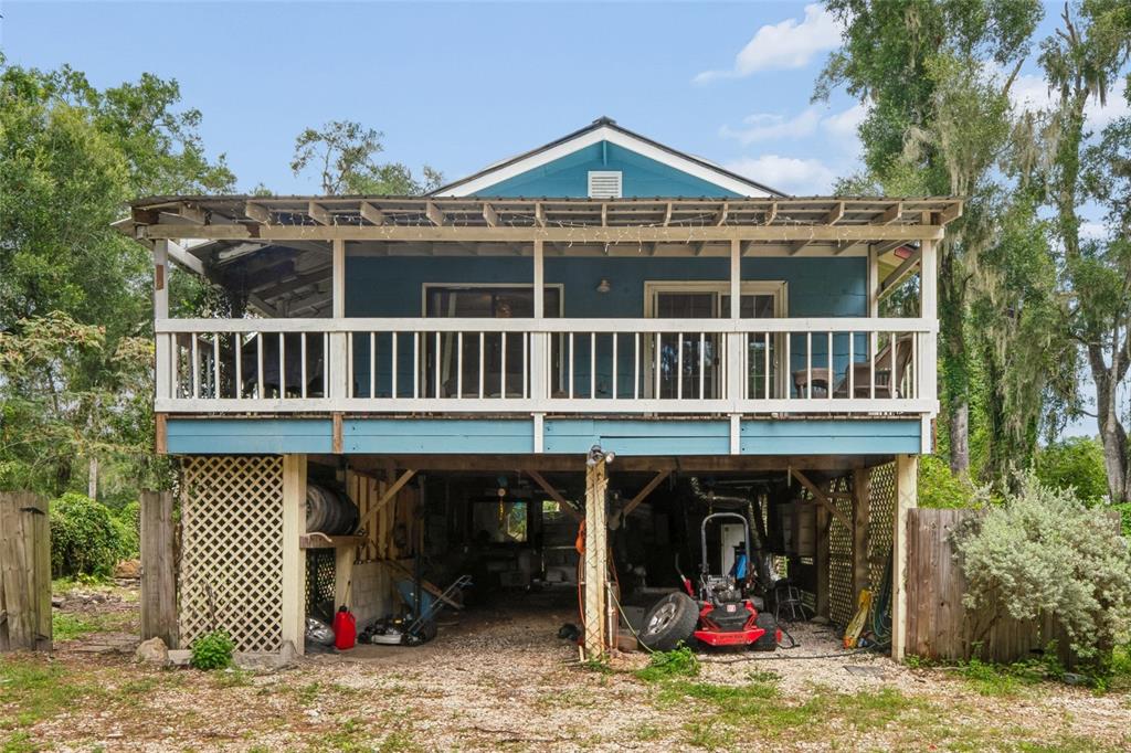 A blue elevated house features a large wooden deck and an open-air ground level storage area — 25141 KIBLER LANE, BROOKSVILLE, FL