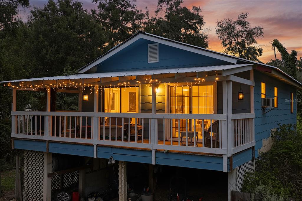 A blue elevated house with a wooden porch and string lights at sunset — 25141 KIBLER LANE, BROOKSVILLE, FL