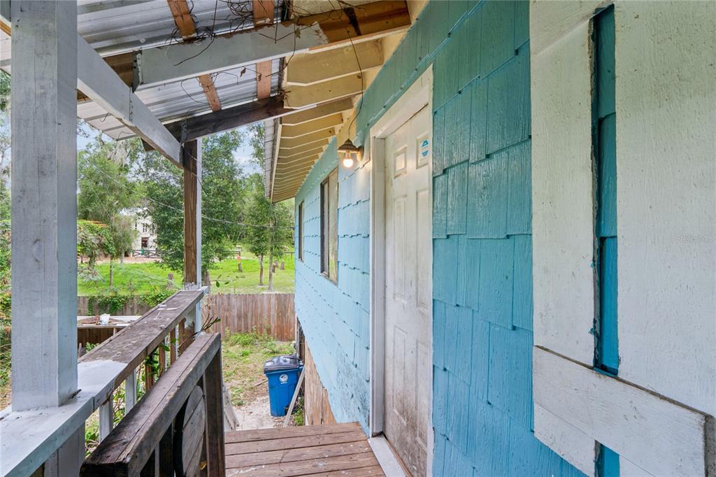 A wooden porch with a blue shingled wall leads to a white door under a roof — 25141 KIBLER LANE, BROOKSVILLE, FL