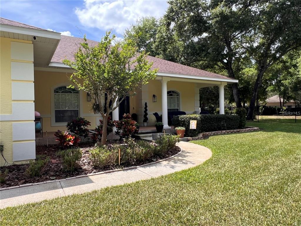 A yellow house with a covered front porch, a curved walkway, and mature landscaping — 52 PINE FOREST DRIVE, HAINES CITY, FL