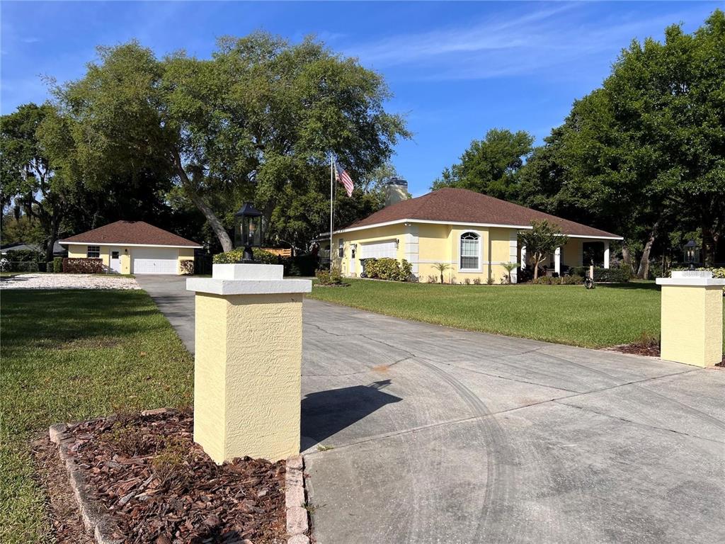 A yellow house with a detached garage sits behind a concrete driveway and pillars — 52 PINE FOREST DRIVE, HAINES CITY, FL