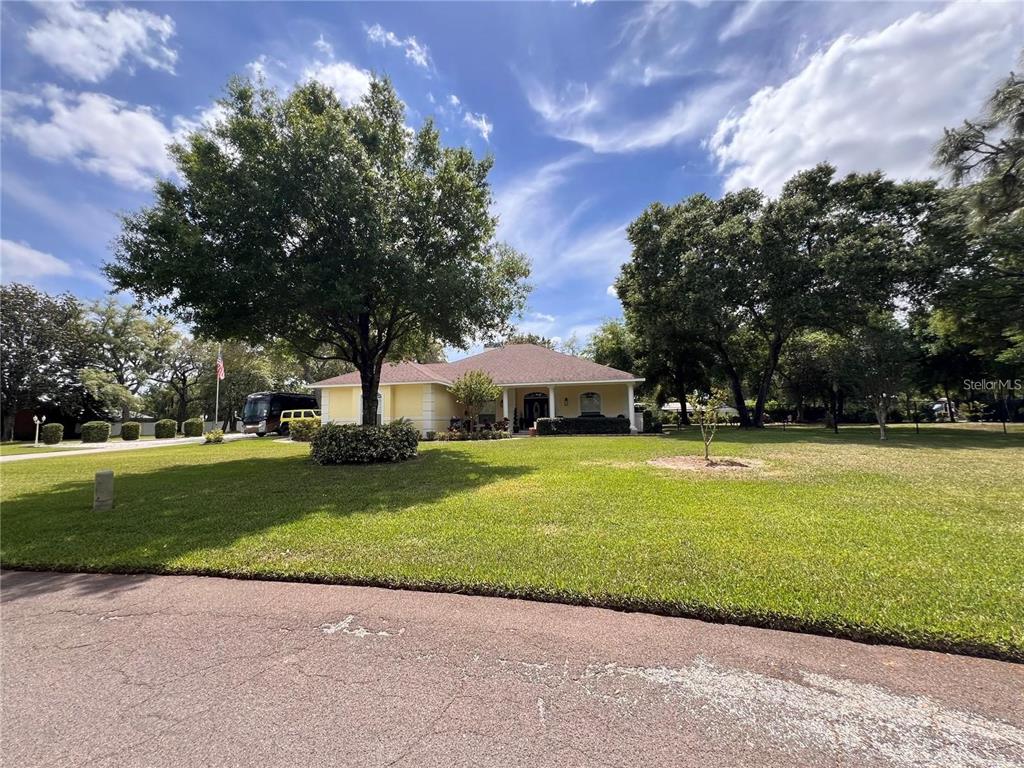 A single-story house with a light-colored exterior sits behind a large lawn and mature trees — 52 PINE FOREST DRIVE, HAINES CITY, FL