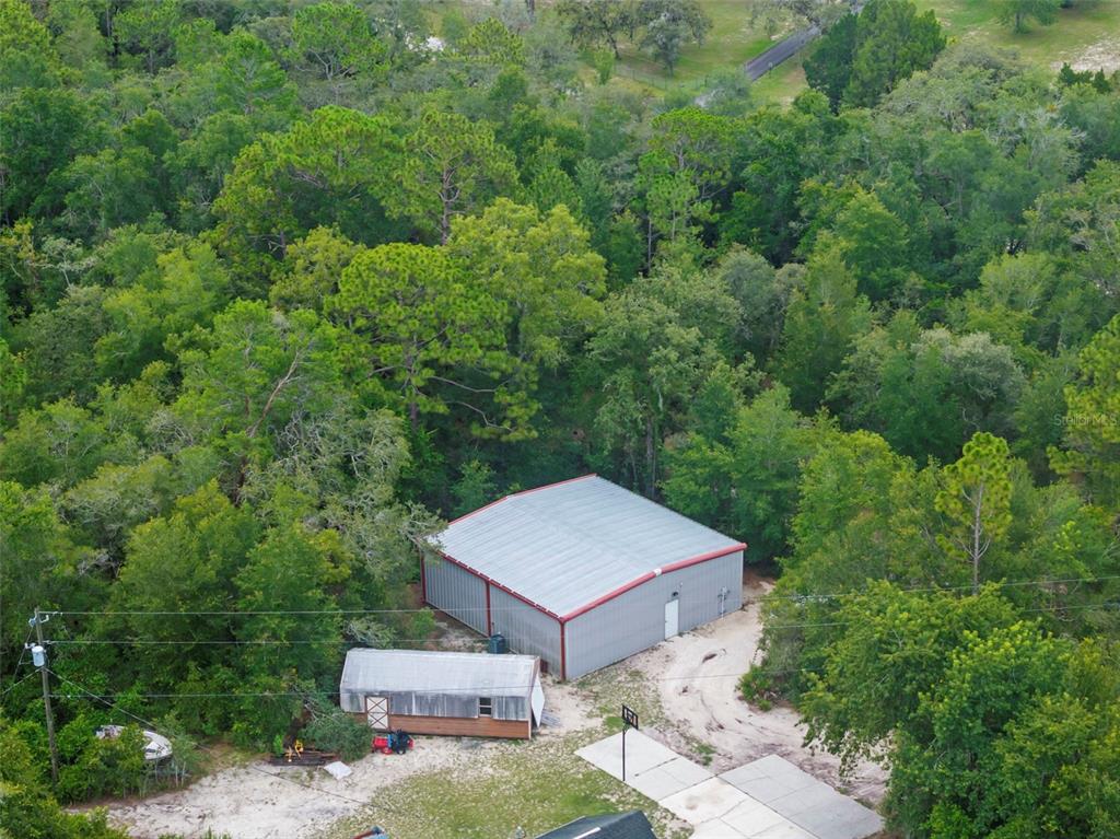 An aerial view shows a large metal workshop and a smaller shed surrounded by trees — 17131 DALBERG DRIVE, SPRING HILL, FL