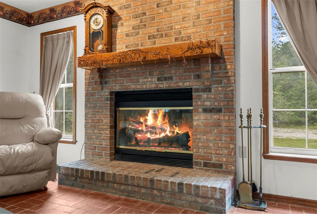 A brick fireplace with a wooden mantel and a clock sits between two windows — 17131 DALBERG DRIVE, SPRING HILL, FL