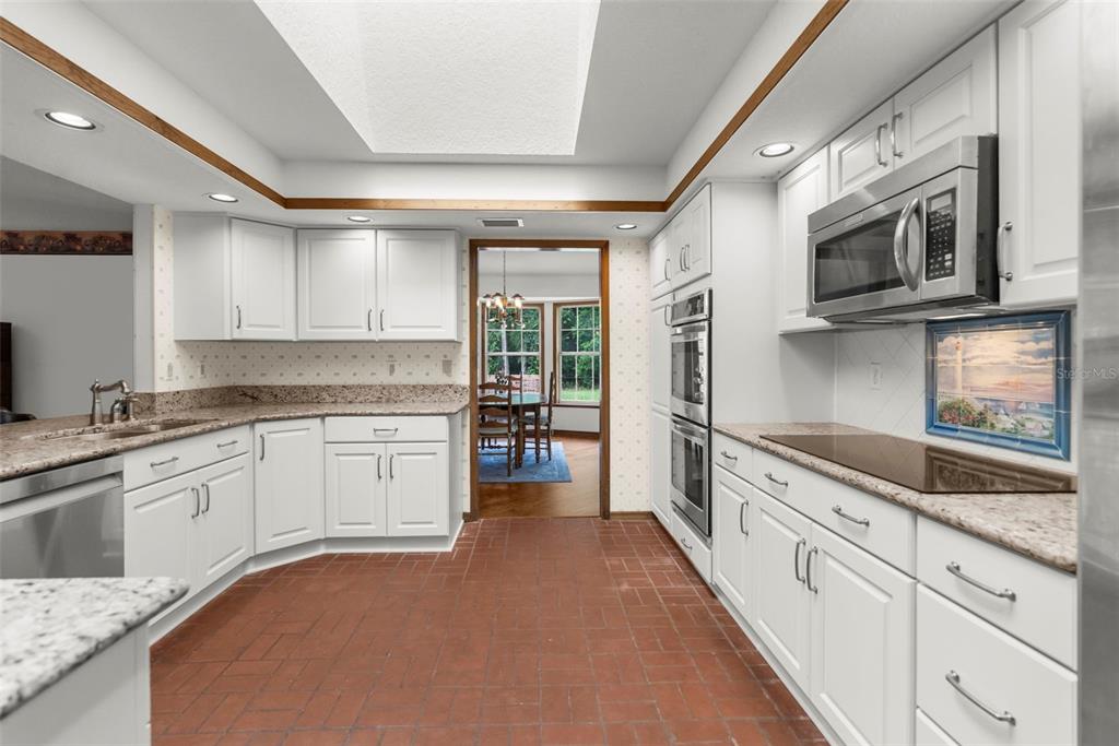 A kitchen with white cabinets, granite countertops, a skylight, and red tile flooring — 17131 DALBERG DRIVE, SPRING HILL, FL