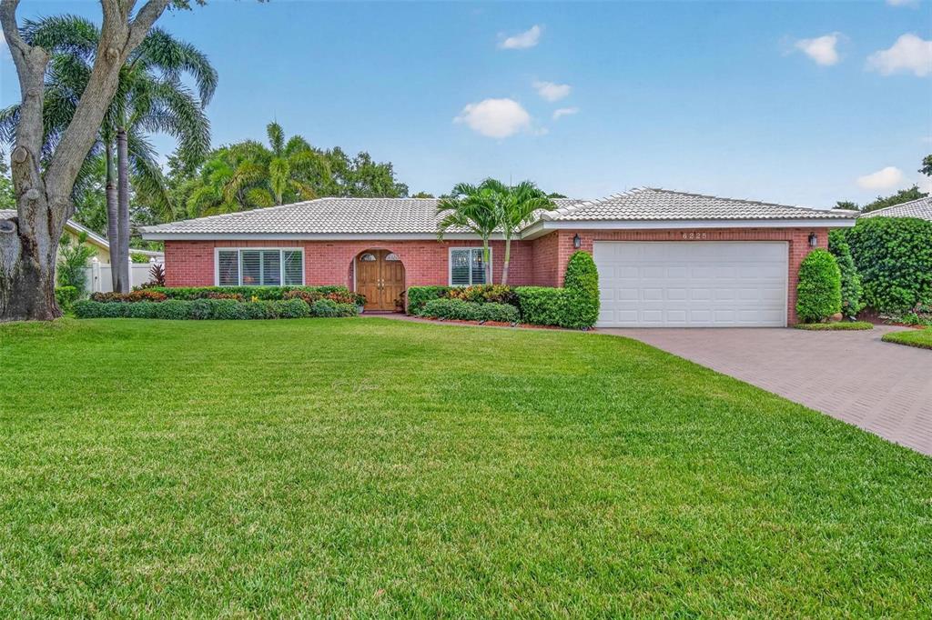 A single-story brick house with a white tile roof, a two-car garage, and a lawn — 6225 43RD AVENUE N, KENNETH CITY, FL