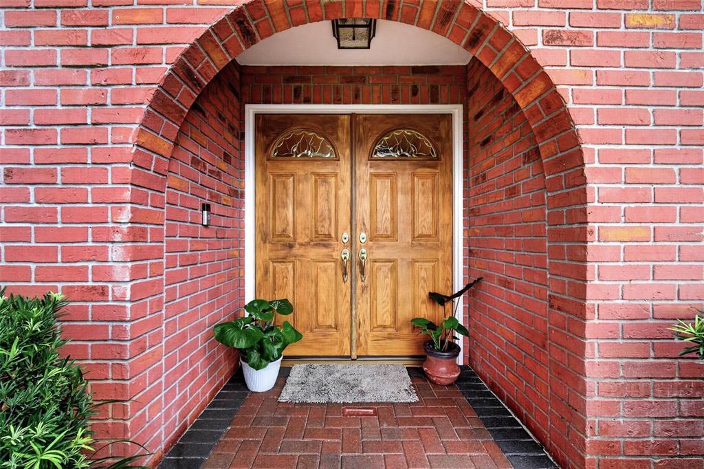A brick arched entryway features double wooden doors with glass inserts and potted plants — 6225 43RD AVENUE N, KENNETH CITY, FL