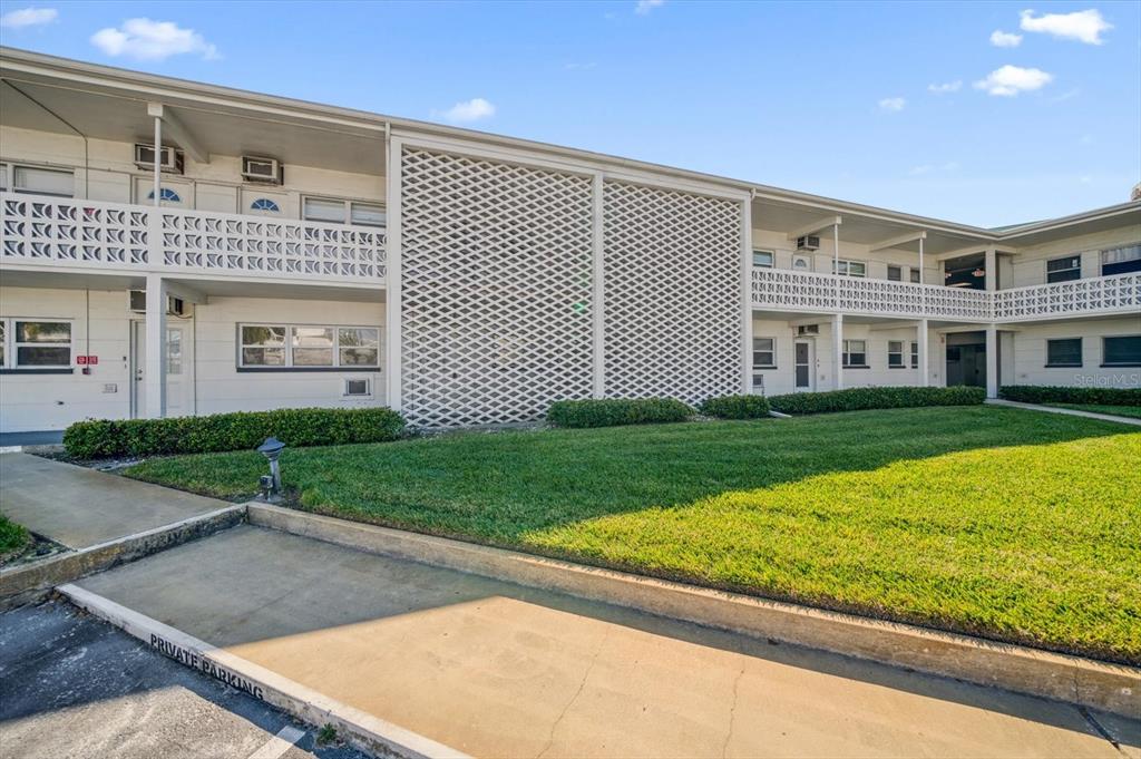 A two-story apartment building features a white lattice facade and a private parking space — 7050 SUNSET WAY UNIT 6, ST PETE BEACH, FL