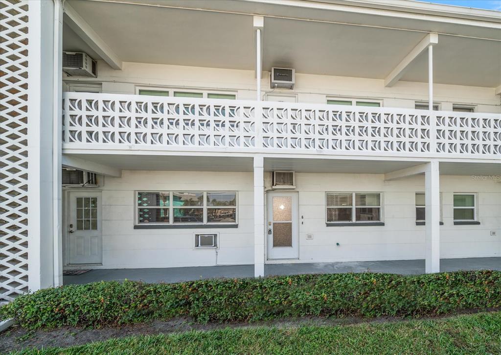 A two-story apartment building exterior features white walls, a decorative breeze block railing, and walkways — 7050 SUNSET WAY UNIT 6, ST PETE BEACH, FL