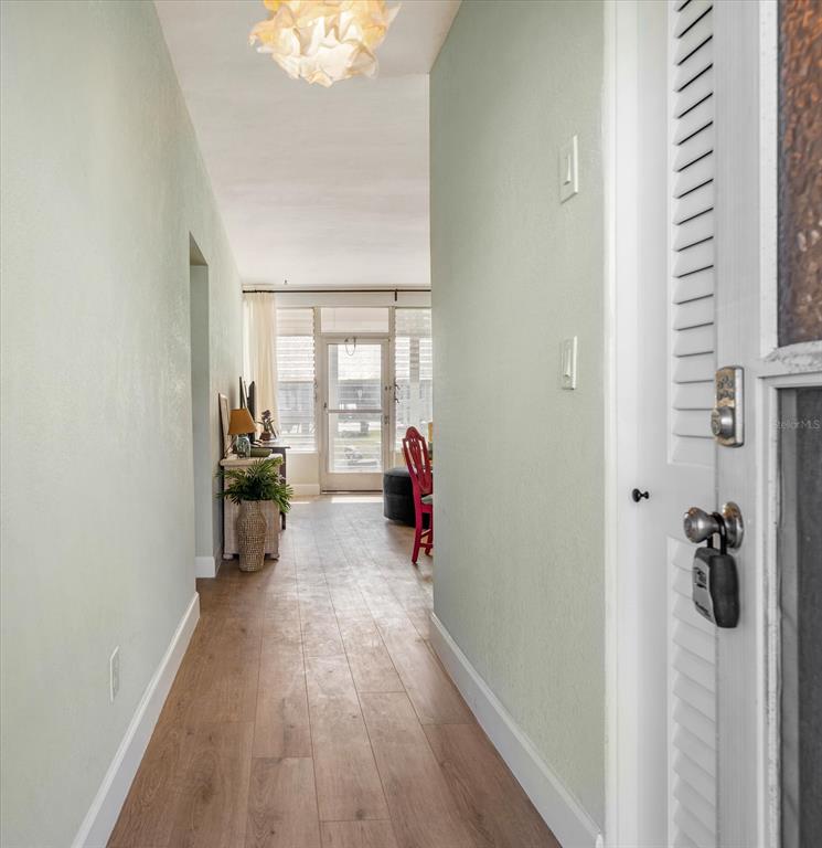 A hallway with light green walls and wood-look flooring leads toward a bright living area — 7050 SUNSET WAY UNIT 6, ST PETE BEACH, FL