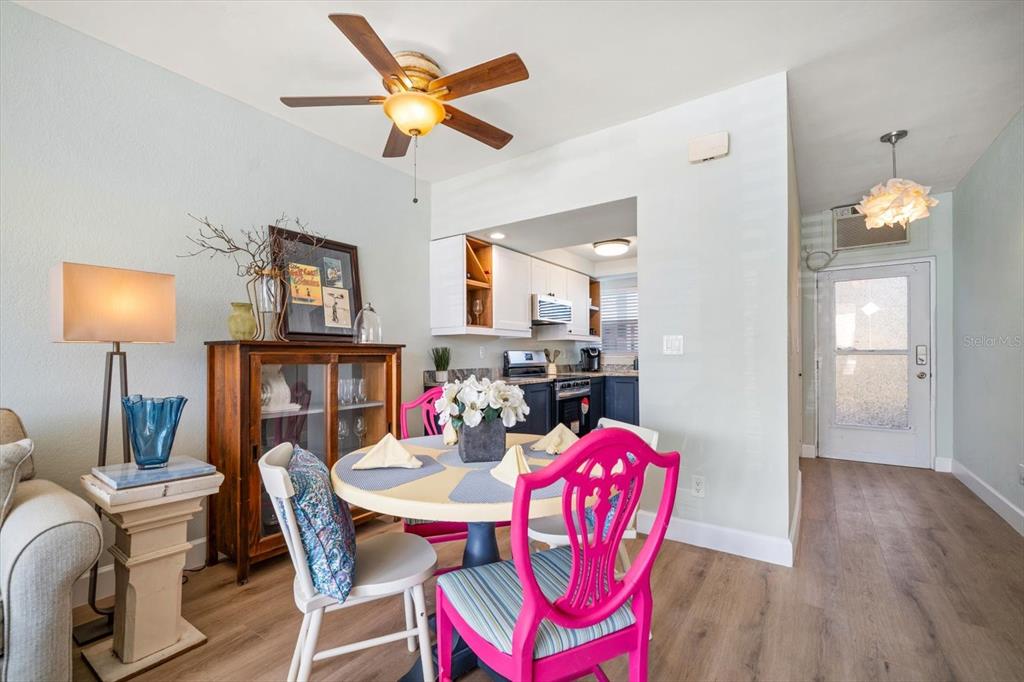 A dining area with a round table, bright pink chairs, and an adjacent kitchen — 7050 SUNSET WAY UNIT 6, ST PETE BEACH, FL