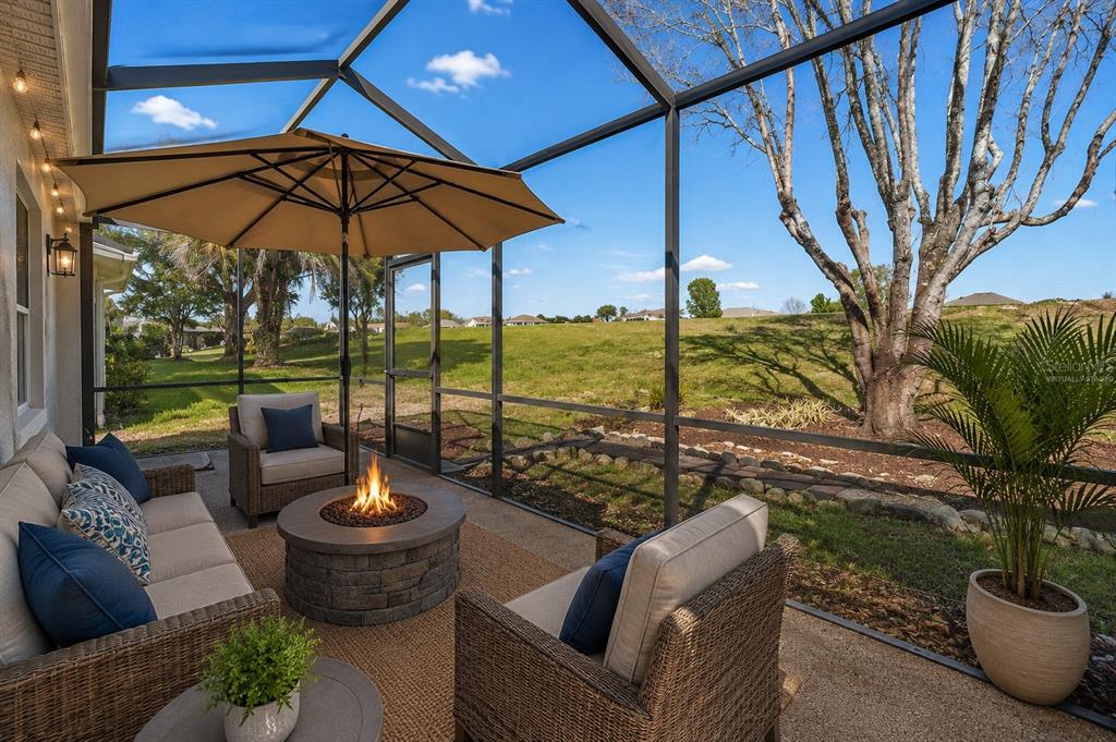 A screened-in patio features a fire pit, outdoor furniture, and views of a grassy yard — 11614 SE 172ND LOOP, SUMMERFIELD, FL