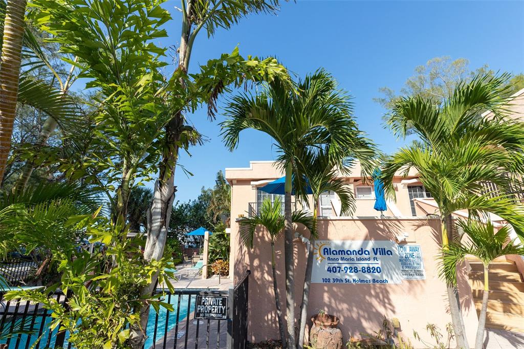 A swimming pool area with palm trees and a building sign at a villa — 102 39TH STREET UNIT 2, HOLMES BEACH, FL