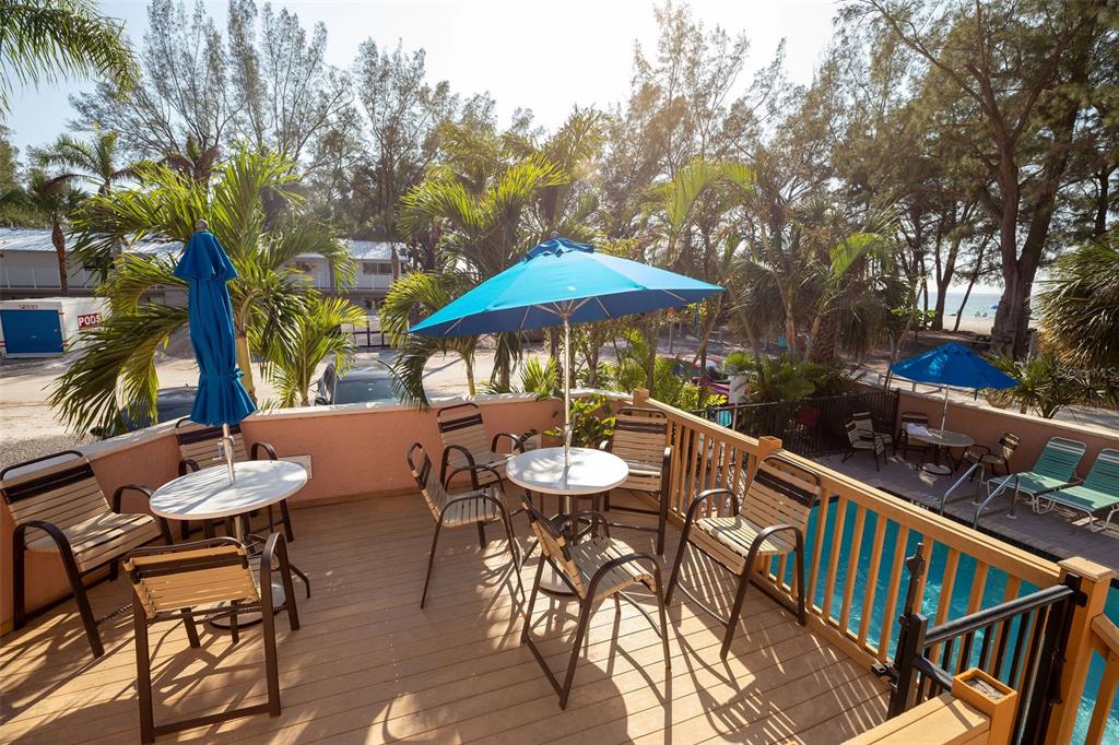 An elevated wooden deck features patio tables with blue umbrellas overlooking a swimming pool — 102 39TH STREET UNIT 2, HOLMES BEACH, FL