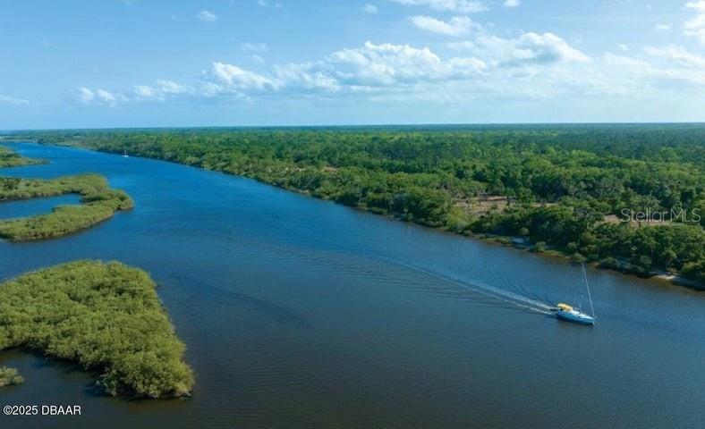 An aerial view shows a sailboat traveling along a river bordered by dense green forest — 93 CORONADO ROAD, FLAGLER BEACH, FL
