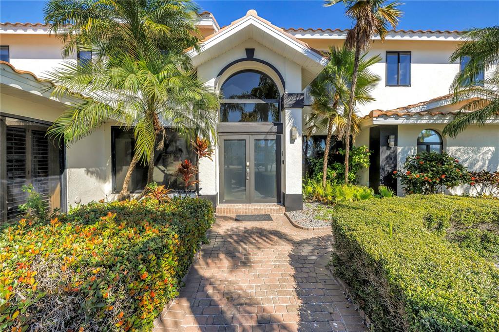 A brick walkway leads to the double front doors of a two-story stucco house — 583 CRYSTAL DRIVE, MADEIRA BEACH, FL