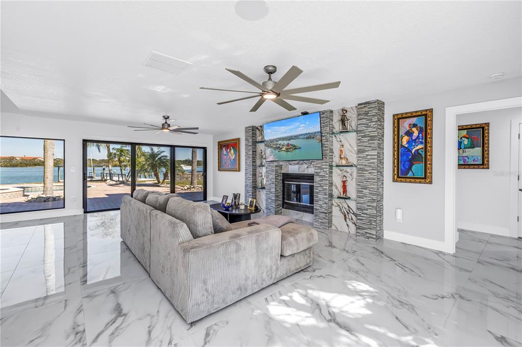 A living room with marble floors, a stone fireplace, and sliding doors overlooking the water — 583 CRYSTAL DRIVE, MADEIRA BEACH, FL