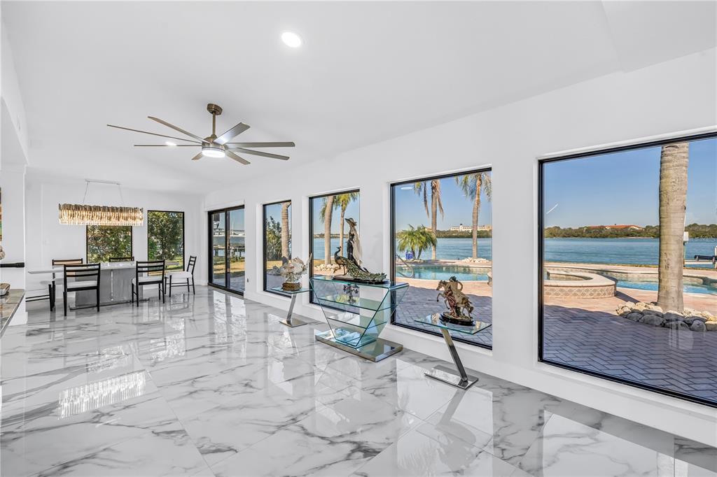 A bright room with white marble floors, a ceiling fan, and large windows overlooking a pool — 583 CRYSTAL DRIVE, MADEIRA BEACH, FL