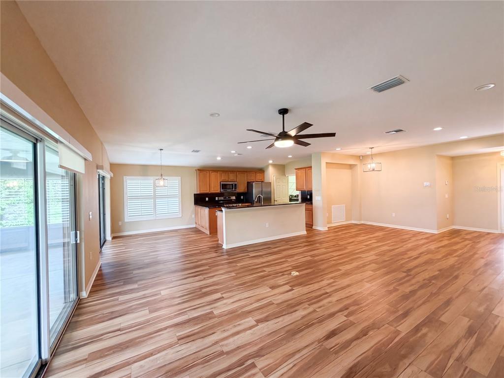 An open-concept living area features wood-look flooring, a kitchen with wooden cabinets, and sliding doors — 13940 SE 95TH COURT, SUMMERFIELD, FL