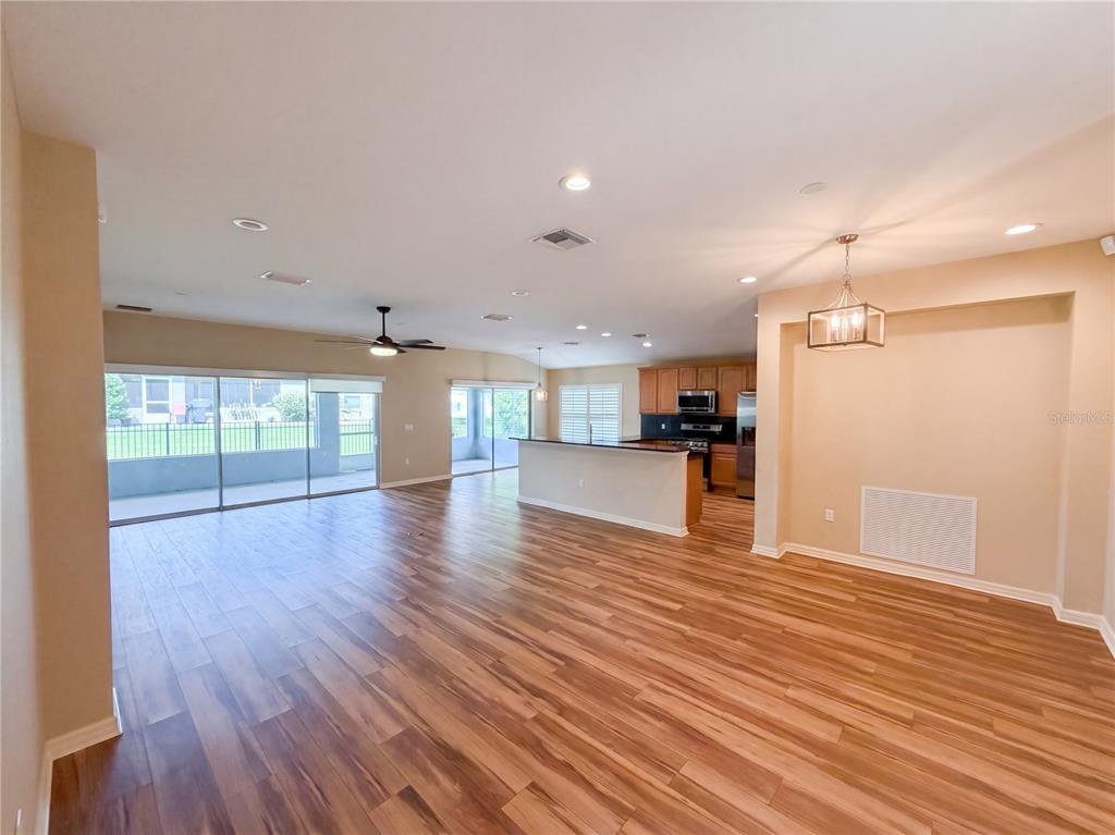 An open-concept living and dining area features wood-look flooring, a kitchen island, and sliding doors — 13940 SE 95TH COURT, SUMMERFIELD, FL