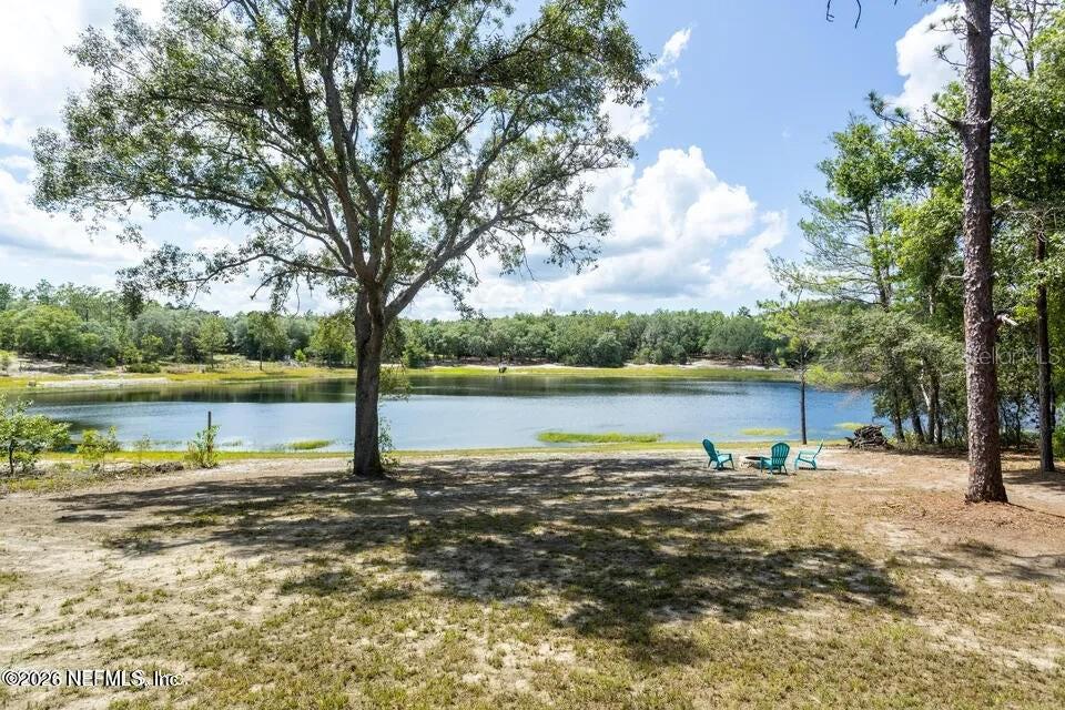 A grassy yard with large trees overlooks a lake with three chairs near the shore — 168 HOUR GLASS CIRCLE, HAWTHORNE, FL