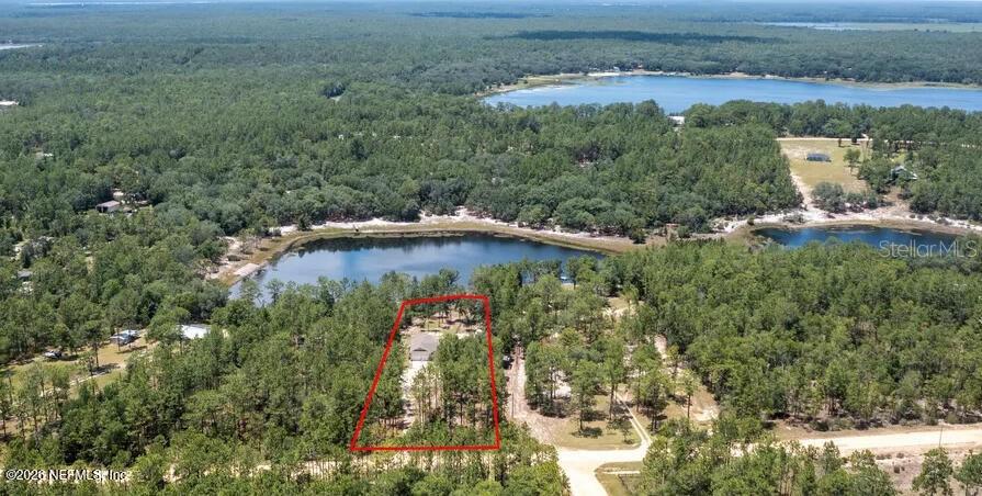 An aerial view shows a house situated on a wooded lot near a lake — 168 HOUR GLASS CIRCLE, HAWTHORNE, FL