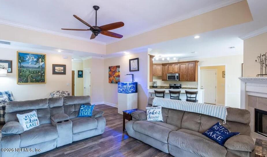 This open-concept living room features wood-look flooring, two gray sofas, and a kitchen in the background — 168 HOUR GLASS CIRCLE, HAWTHORNE, FL