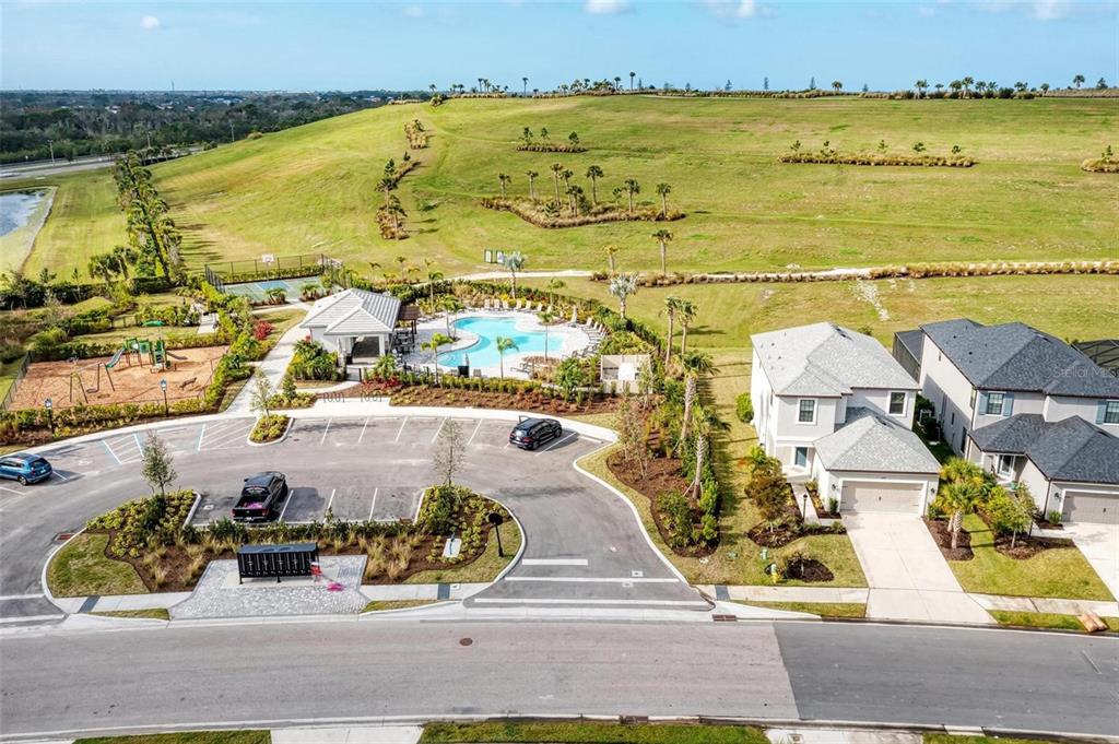 An aerial view shows a community pool, playground, and houses near a large grassy hill — 5564 SUMMIT GLEN, BRADENTON, FL